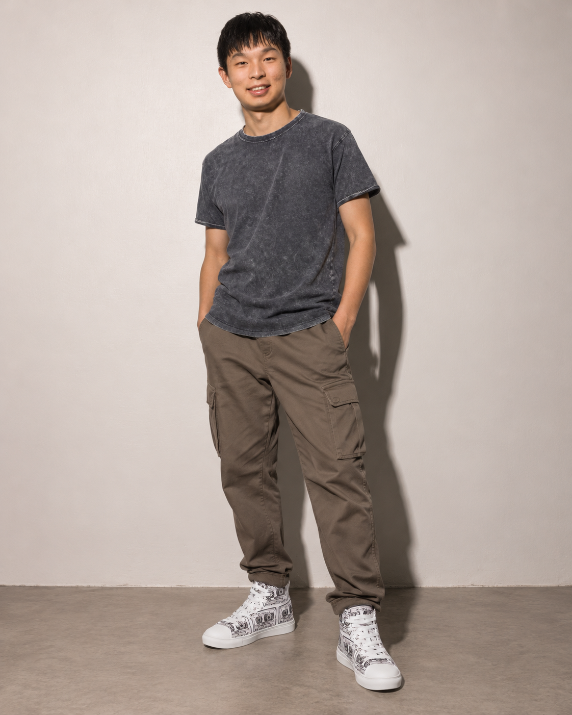 A man wearing Vicky Steane's Mix Tape white sneakers with black cassette hand drawn patterns, standing against a plain light gray wall.