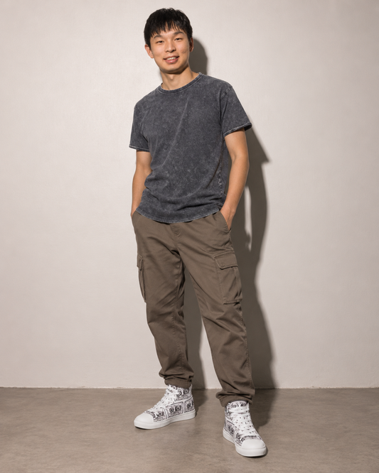 A man wearing Vicky Steane's Mix Tape white sneakers with black cassette hand drawn patterns, standing against a plain light gray wall.